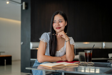 An attractive Asian woman is sitting in a coffee shop, looking out the window while daydreaming.