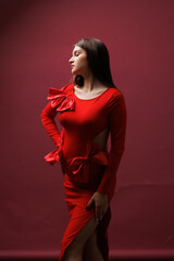 Beautiful young pregnant brunette girl. A woman waiting for a baby in a red dress with bows, on red background, in the studio. 