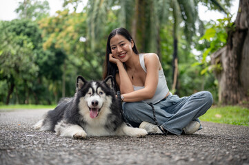 A Siberian husky dog and its owner are smiling at the camera while sitting together in a park. © bongkarn