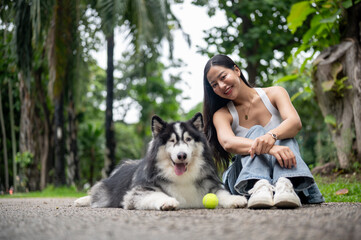 A woman smiles at the camera while sitting on a street in a park, with her dog lying nearby.