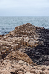 Basalt columns at the Giant Causeway in Northern Ireland form a unique natural pattern by the ocean. The hexagonal rock formations create a stair like appearance along the rugged coast