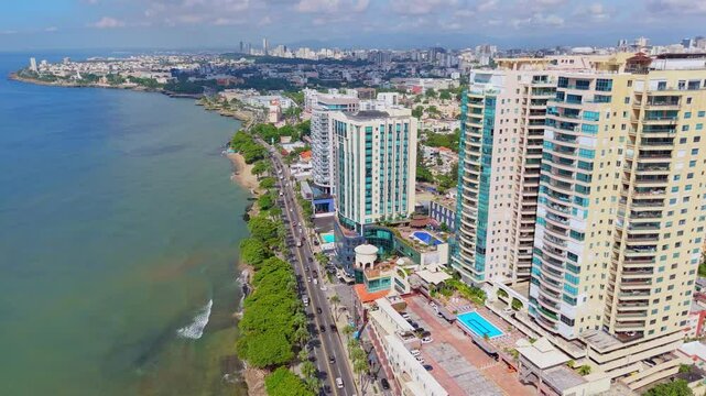 Half-circle aerial shot over the Malecon in Santo Domingo, showcasing George Washington Avenue, coastal buildings, traffic, and ocean waves.