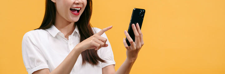 Woman reading good news on smartphone with excited face and enjoying isolated on yellow background