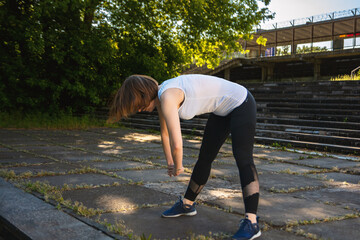 An adult woman is doing fitness in the park. The woman is bending forward.