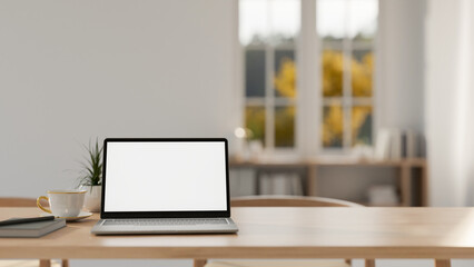 A laptop with a white screen mockup on a wooden tabletop in a contemporary minimalist room.