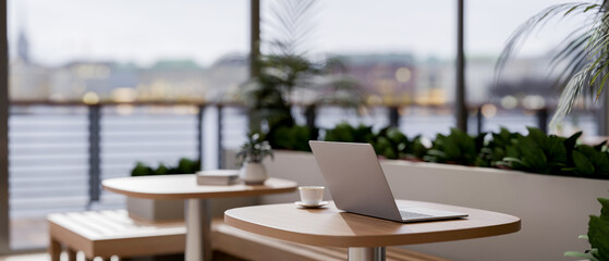 A laptop on a wooden table in a contemporary coffee shop or restaurant with a stunning city view.