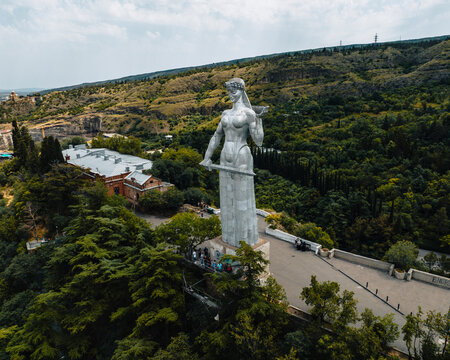 Aerial view of the iconic mother of georgia statue overlooking the scenic betlemi historic quarter with hills and greenery, tbilisi, georgia.
