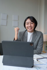 Happy young woman, successful businesswoman feeling delighted with good news received online from laptop, tablet on desk in modern office.