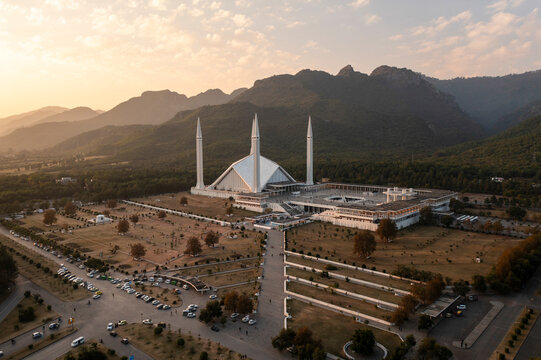 Aerial view of faisal masjid mosque surrounded by majestic mountains and serene trees at sunset, islamabad, pakistan.