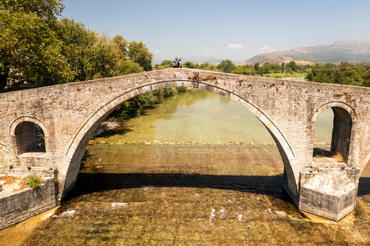 Aerial view of the picturesque stone bridge over a scenic river surrounded by beautiful mountains and greenery, Arta, Greece.