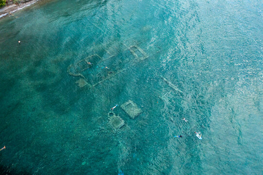 Aerial view of underwater ruins in clear blue sea with swimmers, Archea Epidavros, Greece.