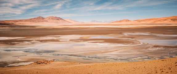 The Quisquiro Salt Flat showcases its vast, flat terrain in the beautiful altiplano of Puna de Atacama, near San Pedro de Atacama in Chile, reflecting a mix of blues and browns under a bright sky