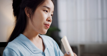 Portrait of Relaxed female freelancer having snack during video conference with team members via laptop in home office. Work from home, remote working.