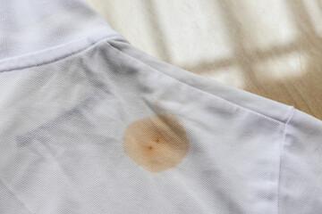 Patch of brown stain on white t-shirt laid on table before laundry