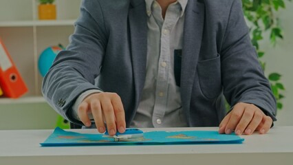 A man sits in a travel agency office and shows a close up of an airplane flying over a map.