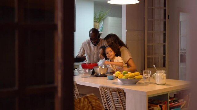 Happy multiethnic family together little mixed race daughters cooking pancakes mix dough and healthy food in modern kitchen evening. Smiling multiracial family preparing with adorable small diverse