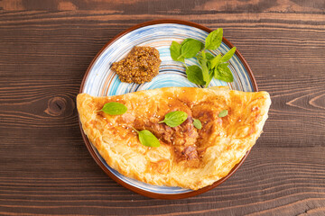 Fried homemade khachapuri cake with cheese and meat, fried in pan on brown wooden. Side view, copy space.