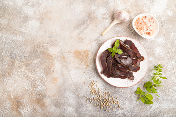 Armenian Basturma dried meat on plate with pepper and herbs on brown concrete. Top view, copy space.