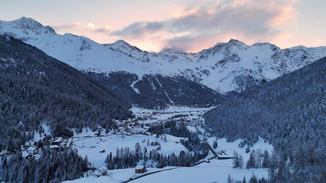 Aerial drone shot (reversing) of the wintry Sulden valley in the European Alps at sunrise