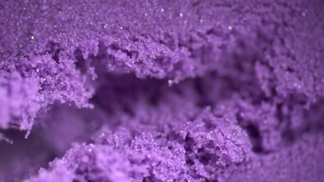 Metal spatula touching the purple kinetic sand. Textured, crumbly kinetic sand in lavender color. Kinetic sand background