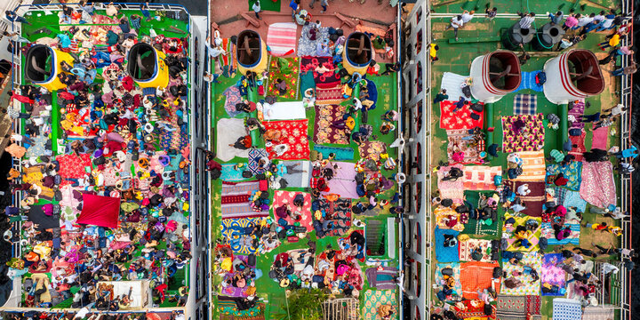 Aerial view of colorful crowds of people waiting on rooftops of ferries on the bustling Buriganga River during Eid celebrations, Keraniganj, Bangladesh.