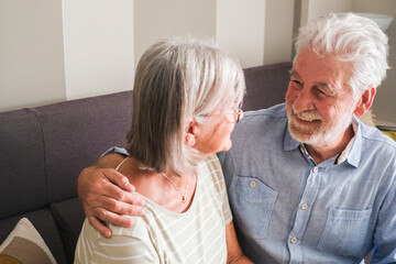 Heartwarming moment of an elderly couple sitting on a cozy sofa at home, smiling and sharing tender words. Captures the essence of mature love, mutual care, and the happiness of togetherness in later