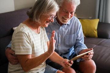 Mature couple using a tablet device for a video call with family or friends, enjoying modern technology. Elderly grandparents have fun interacting online, showcasing their engagement with the internet