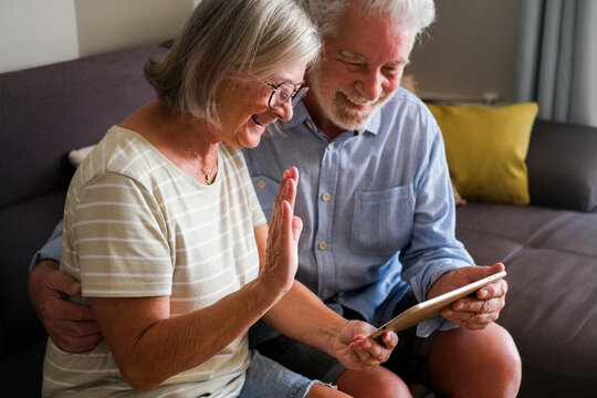 Mature couple using a tablet device for a video call with family or friends, enjoying modern technology. Elderly grandparents have fun interacting online, showcasing their engagement with the internet