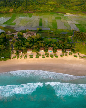 Aerial view of luxury resort by the beautiful beach at sunset with rice fields, Pantai Marosi, Sumba, Indonesia.