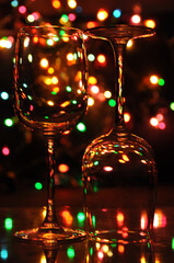 Two transparent wine glasses filled with water, with colorful Christmas lights on a tree in the background