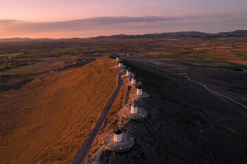 Aerial view of traditional windmills at sunrise with a scenic road in the picturesque countryside, Consuegra, Spain.