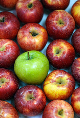 Top view a collection of many red apples with one distinct green apple in the center. The contrast between the single green apple and the surrounding red apples makes this image visually striking