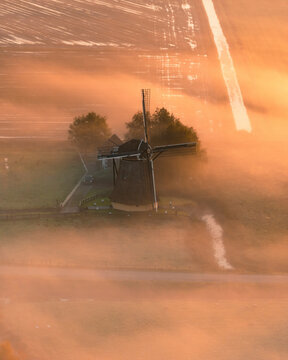 Aerial view of a traditional windmill surrounded by fog at sunrise, Workum, Friesland, Netherlands.