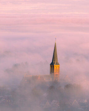 Aerial view of a serene city shrouded in fog with a church at sunrise, Workum, Netherlands.