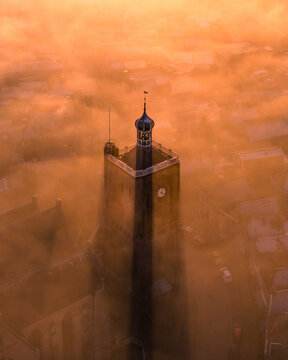 Aerial view of a mystical cityscape with a church tower emerging from fog and low clouds at sunrise, Workum, Friesland, Netherlands.