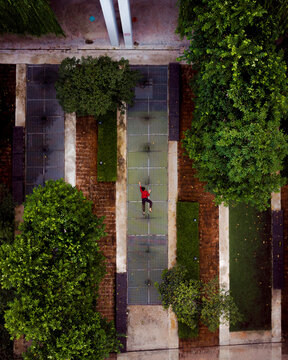 Aerial view of a peaceful urban garden with a woman walking along a pathway surrounded by greenery and modern apartments at sunrise, Cyberjaya, Malaysia.