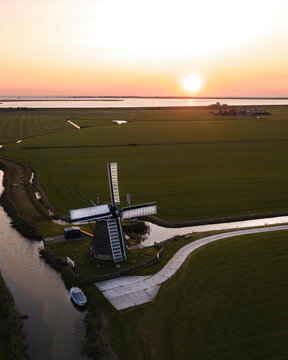 Aerial view of cornwerder molen windmill at sunset with a serene river and sailing boat, Cornwerd, Netherlands.