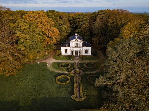 Aerial view of a beautiful house surrounded by a serene forest and vibrant garden during autumn sunset, Oudemirdum, Netherlands.