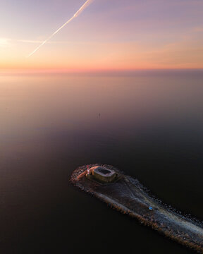 Aerial view of a serene bunker by the tranquil IJsselmeer lake at sunrise, Afsluitdijk, Netherlands.