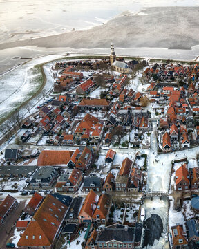 Aerial view of a picturesque winter wonderland village with snow-covered rooftops and a frozen canal, Hindeloopen, Netherlands.