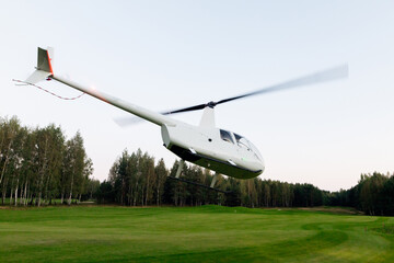 Helicopter flying over a green field surrounded by trees during dusk in a serene landscape concept