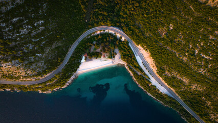 Aerial view of a serene beach along the Adriatic Sea with a winding road and mountains at sunset, Dubravica, Croatia.