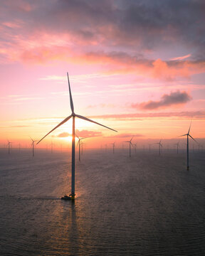Aerial view of offshore windpark with wind turbines and a boat at sunrise over IJsselmeer lake, Afsluitdijk, Netherlands.