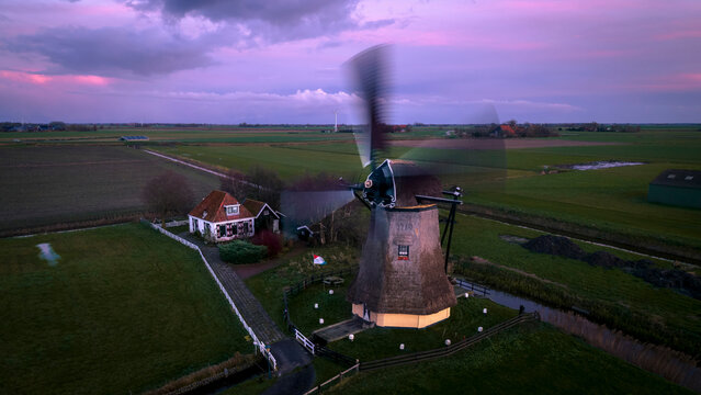 Aerial view of a picturesque windmill at sunrise surrounded by serene fields and a traditional farmhouse, Workum, Netherlands.