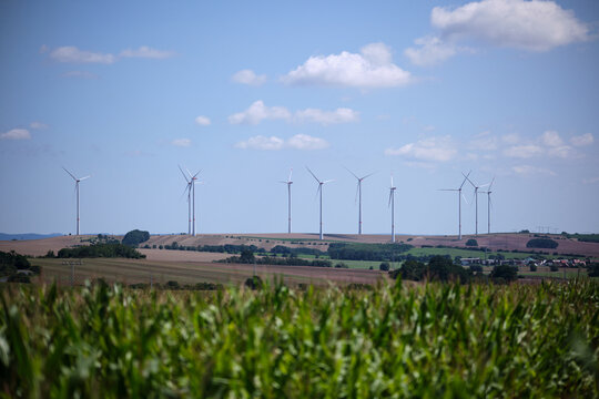 Green cornfield and wind power turbine against a blue sky with white clouds. Renewable energy source. Powerful and ecological energy concept