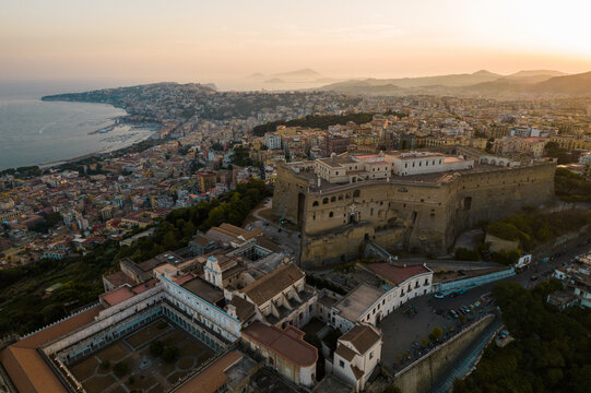 Aerial view of vibrant cityscape with historic castle and coastline at sunset, Vomero Hill, Naples, Italy.