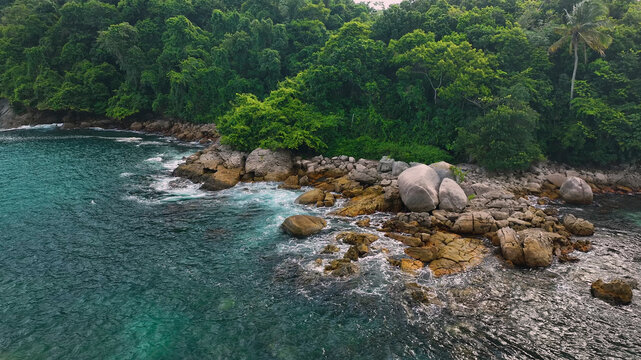 Aerial view of beautiful tropical coastline with clear blue ocean, lush greenery, and rocky shore, Ubatuba, Brazil.