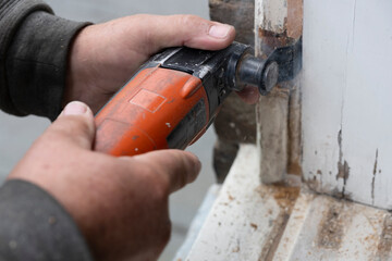 Carpenter cuts a piece of rotten wood from a window frame with an oscillating renovator saw, the unique system for remodeling and renovation