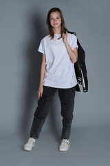 A teenage girl stands confidently with a jacket draped over her shoulder, wearing a simple white...