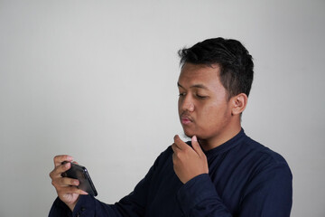 Southeast Asian man wearing navy blue shirt watching on his mobile phone